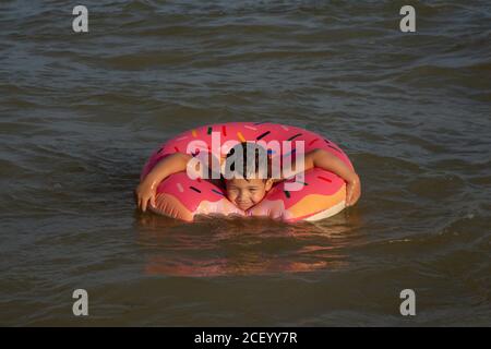 Un garçon de 5 ans nage dans la mer, se réjouit et s'amuse dans un anneau gonflable en forme de donut. Banque D'Images