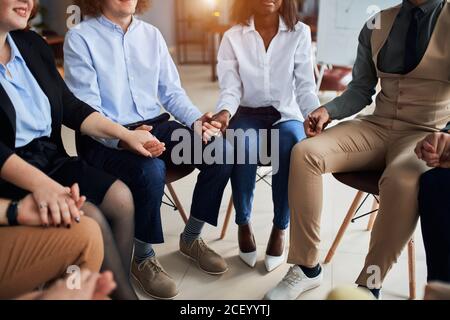 Divers dirigeants, collègues et équipes d'affaires tiennent les mains ensemble tout en étant assis sur des chaises en cercle, portant des vêtements formels. Les gens d'affaires créatifs concparviennent Banque D'Images