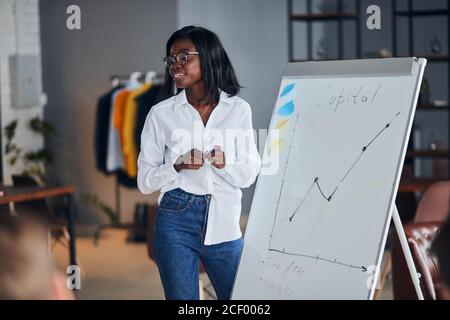 Une femme d'affaires africaine confiante en chemise blanche et en jeans bleus explique comment faire une présentation de tableau de conférence pour les jeunes leaders, partager le bussin Banque D'Images