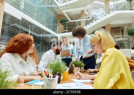 Assez concentrée femme débutant regarde avec des expressions attentives, écrit les informations nécessaires, se tient derrière le chef d'équipe occupé en roo Banque D'Images