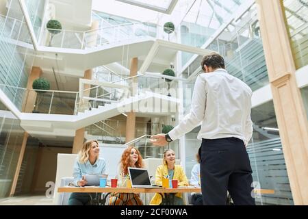 Un noble et agréable chef d'équipe se tient devant des partenaires heureux avec dos à la caméra, discute de nouveau projet de conception dans un bureau moderne lumineux, tourné Banque D'Images