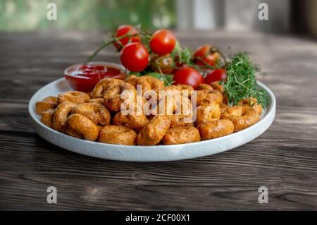Tortellini fait à la main avec des tomates et des verts de thym sur une plaque blanche est appelé taralli. Taralli dans les boulangeries italiennes dans le sud de l'Italie sur un bois Banque D'Images