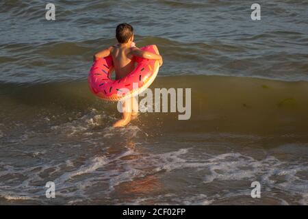 Un garçon de 5 ans nage dans la mer, se réjouit et s'amuse dans un anneau gonflable en forme de donut. Banque D'Images