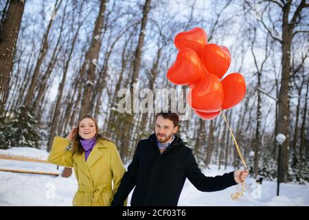 jeune et beau couple caucasien ayant la promenade. romantique homme et femme en manteaux datant, tenir les ballons d'air rouges dans les mains, ils semblent heureux togethe Banque D'Images