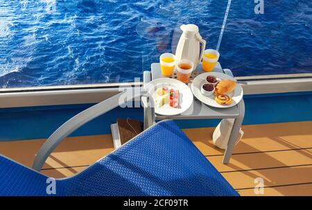 Un petit-déjeuner continental coloré est servi sur le balcon d'un bateau de croisière en mer, avec des fruits, des jus de fruits, du pain et du café. Banque D'Images