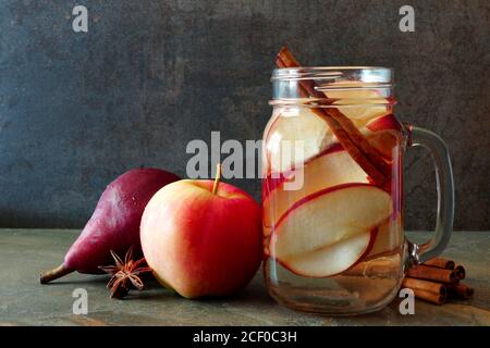 Eau de détox sur le thème de l'automne avec pomme, cannelle et poire rouge dans un pot de maçon sur fond d'ardoise sombre Banque D'Images