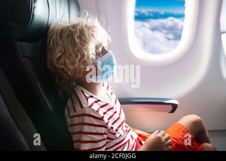 Enfant dans un avion dans un masque et un écran facial. Vol avec des enfants pendant une épidémie virale. Vacances en coronavirus et pandémie de grippe. Voyager en toute sécurité avec le jeune CH Banque D'Images