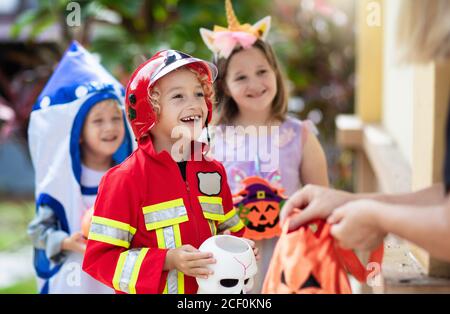 Les enfants se déguent en costume d'Halloween. Les enfants de couleur s'habillent avec un seau à bonbons dans la rue de banlieue. Petit garçon et fille trick ou traiter le wi Banque D'Images