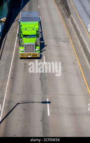 Vert vif industriel classique américain grand camion semi-porteur avec pièces chromées et signe de charge surdimensionnée sur le pare-chocs avant transport de la charge sur un chariot à plateau Banque D'Images