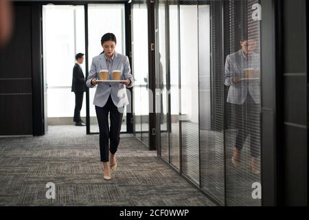 jeune stagiaire asiatique portant un plateau de tasses de café dans le bureau de l'entreprise Banque D'Images