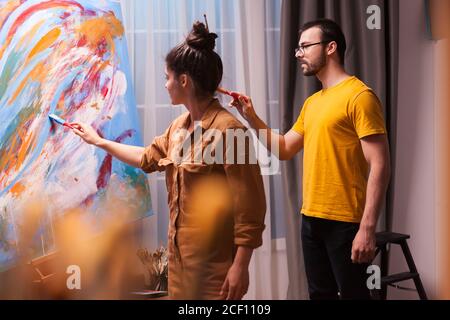 Homme et femme peignant ensemble sur une grande toile dans un studio d'art. Peinture d'art moderne sur toile, art créatif, contemporain et réussi dessin d'artiste chef-d'œuvre Banque D'Images