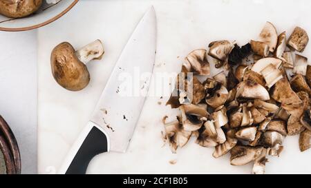 Petits champignons bella bio frais, frais et crus, hachés, gros plan sur une planche à découper en marbre, à plat Banque D'Images