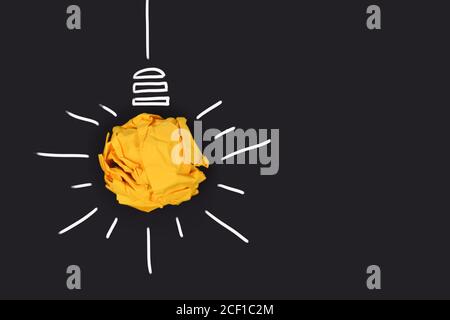 Idée concept avec ampoule en papier jaune émietté boule et lignes blanches dessinées sur fond noir foncé Banque D'Images