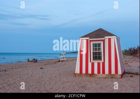 Les gens se détendent sur la plage au coucher du soleil. Enfants jouant dans les eaux peu profondes. Station de secouriste et chaise d'observation. Cavendish Beach, Î.-P.-É., Canada. Banque D'Images