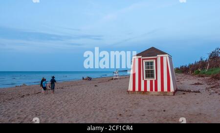 Les gens se détendent sur la plage au coucher du soleil. Enfants jouant dans les eaux peu profondes. Station de secouriste et chaise d'observation. Cavendish Beach, Î.-P.-É., Canada. Banque D'Images