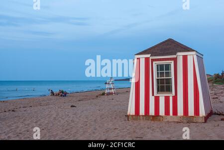 Les gens se détendent sur la plage au coucher du soleil. Enfants jouant dans les eaux peu profondes. Station de secouriste et chaise d'observation. Cavendish Beach, Î.-P.-É., Canada. Banque D'Images