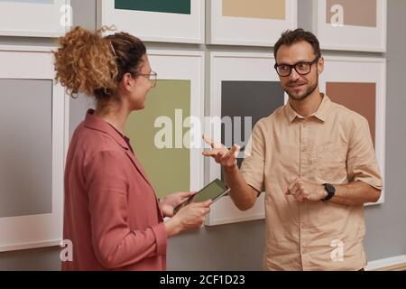 Jeune homme qui parle à une femme en utilisant un PC tablette ils se tiennent contre les photos sur le mur Banque D'Images