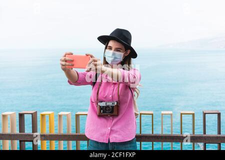 Jeune femme de millénial faisant un vlog avec son smartphone pendant porter un masque de protection pendant son voyage pour la propagation du coronavirus Prévention - taille basse Banque D'Images
