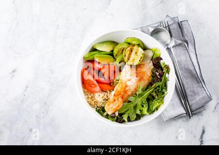 Assiette à salade saine de poisson. Zander, légumes, feuilles vertes, avocat, tomate et riz brun dans un bol Banque D'Images