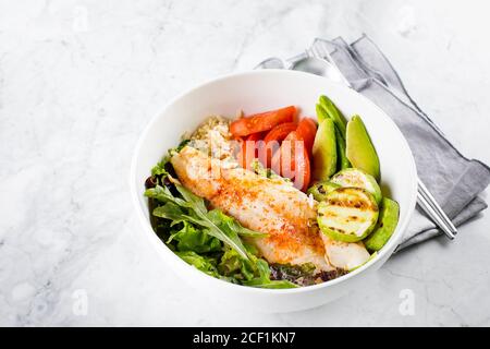 Assiette à salade saine de poisson. Zander, légumes, feuilles vertes, avocat, tomate et riz brun dans un bol Banque D'Images