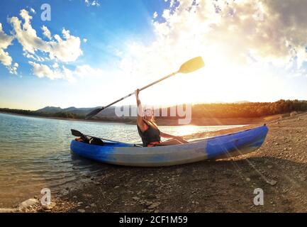 Femme en kayak ramer au paysage marin contre le coucher du soleil à Embalse de la Bolera, Jaen, Espagne. Succès sur le concept des objectifs sportifs. La puissance de la femme. Banque D'Images