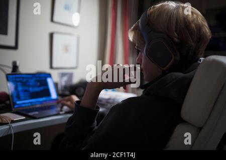 Adolescent avec un casque utilisant un ordinateur dans la chambre sombre Banque D'Images