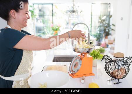 Femme souriante pesant des pommes tranchées pour cuire au four dans la cuisine Banque D'Images