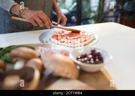 Femme qui répandait de la sauce tomate sur de la pâte à pizza dans la cuisine Banque D'Images