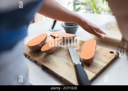 Femme qui coupe des patates douces sur la planche à découper dans la cuisine Banque D'Images