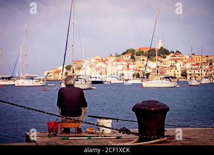 Croatie - coucher de soleil d'été, homme pêchant à partir d'un quai en face de la péninsule de Primosten Banque D'Images