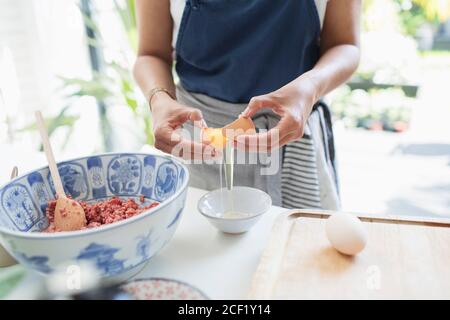 Femme craquant l'œuf sur un bol dans la cuisine Banque D'Images