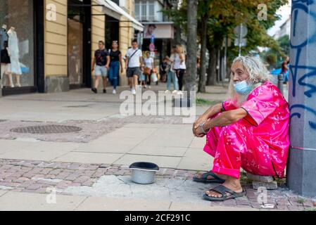 Vieil homme barbu flamboyant avec de longs cheveux blancs et masque facial portant des vêtements roses propres mendiant pour de l'argent dans les rues de Sofia Bulgarie, Balkans Banque D'Images