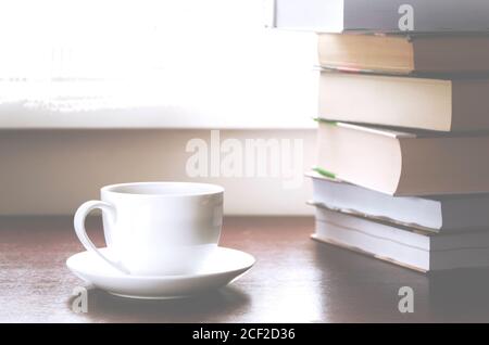 Une tasse de café blanc se trouve sur une table en bois à côté des livres Banque D'Images