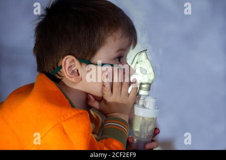 Petit garçon dans un masque, les traitements des voies respiratoires avec  un pulvérisateur à la maison. Siège bébé avec un nébulisateur dans sa  bouche, inhalateur, le traitement de la bronchite Photo Stock 