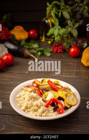 Couscous de porridge avec légumes cuits au four, courgettes et oignons, poivrons et aubergines avec épices, assiette avec nourriture sur fond de bois sombre Banque D'Images