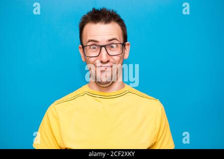 Drôle homme de bande dessinée dans les lunettes fait grimace avec des croix yeux. Jeune homme en t-shirt jaune avec l'expression folle a l'amusement seul, joue imbécile isolé plus Banque D'Images