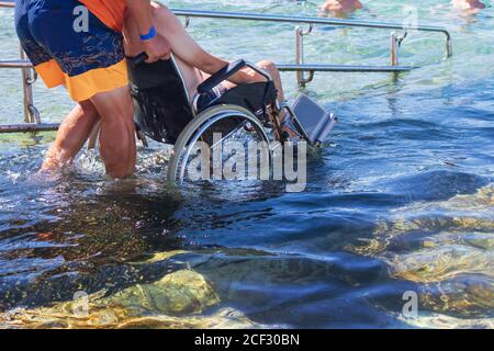 Homme en fauteuil roulant sur la plage accessible avec rampe. Personne handicapée qui va nager. Banque D'Images