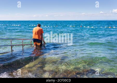 Homme en fauteuil roulant sur la plage accessible avec rampe. Personne handicapée qui va nager. Banque D'Images