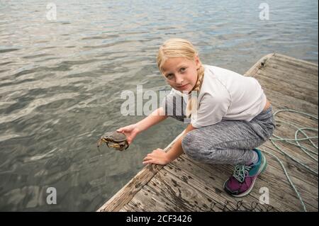 Fille blonde avec tresse tenant un crabe sur un quai en bois Banque D'Images