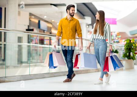 Photo pleine longueur positive joyeuse couple marié homme femme terminez vos achats dans le centre commercial. faites de nombreux bagages les paquets portent des rayures jaunes Banque D'Images