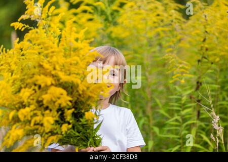 Une petite fille se cacha derrière un bouquet de fleurs jaunes dans un champ. Banque D'Images