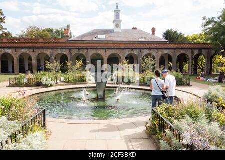 Un couple se tenant à côté de la fontaine Sibirica de William Pye qui s'étend sur un étang dans le jardin de l'iris, Holland Park, à l'ouest de Londres, Royaume-Uni. Banque D'Images