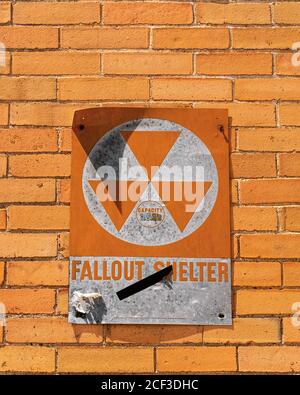 Un panneau orange lumineux vintage lisant Fallout Shelter est accroché à un mur de briques orange. Le signe nous ramène à l'époque de la guerre froide. Selon le tex Banque D'Images