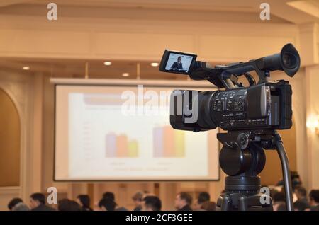 Dans la salle de conférence, la caméra vidéo de gros plan enregistre les discours d'un participant à la conférence sur fond de diagramme et de personnes Banque D'Images