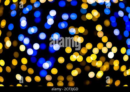 Cercles bokeh bleus et jaunes colorés de Noël du nouvel an illuminations d'arbres avec une vue floue avec effet de flou de flou de défoqué la nuit et arrière-plan noir Banque D'Images