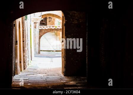 Sienne, Italie ruelle étroite sombre rue vide dans la vieille ville médiévale historique village en Toscane avec personne et passage d'arche Banque D'Images