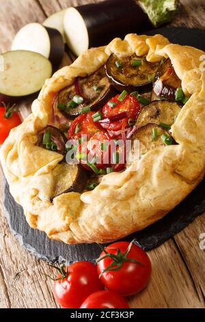 Tarte végétarienne aux aubergines avec tomates, oignons et herbes gros plan sur un tableau d'ardoise sur la table. Verticale Banque D'Images