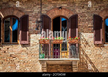 San Gimignano, Italie village ville en Toscane et la clôture de décorations de fleurs rouges sur l'architecture mur de pierre de la maison fenêtre balcon jour d'été Banque D'Images