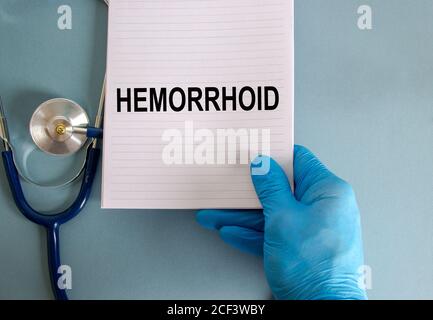 Main dans un gant bleu, carte blanche avec le mot « hémorroïde » et stéthoscope. Magnifique fond bleu. Concept médical. Banque D'Images