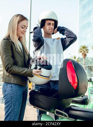 Jeune femme attirante en blouson noir et beau homme régulateur casque et debout autour du scooter vert Banque D'Images
